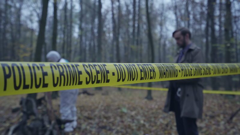 a yellow crime scene tape in front of detectives in a field