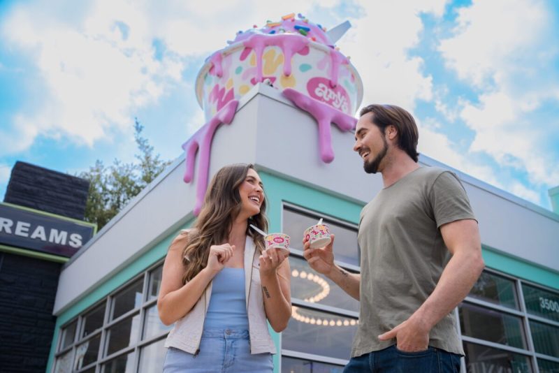 a white woman and man holding cups of ice cream stand outside a houston ice cream shop smiling at each other.